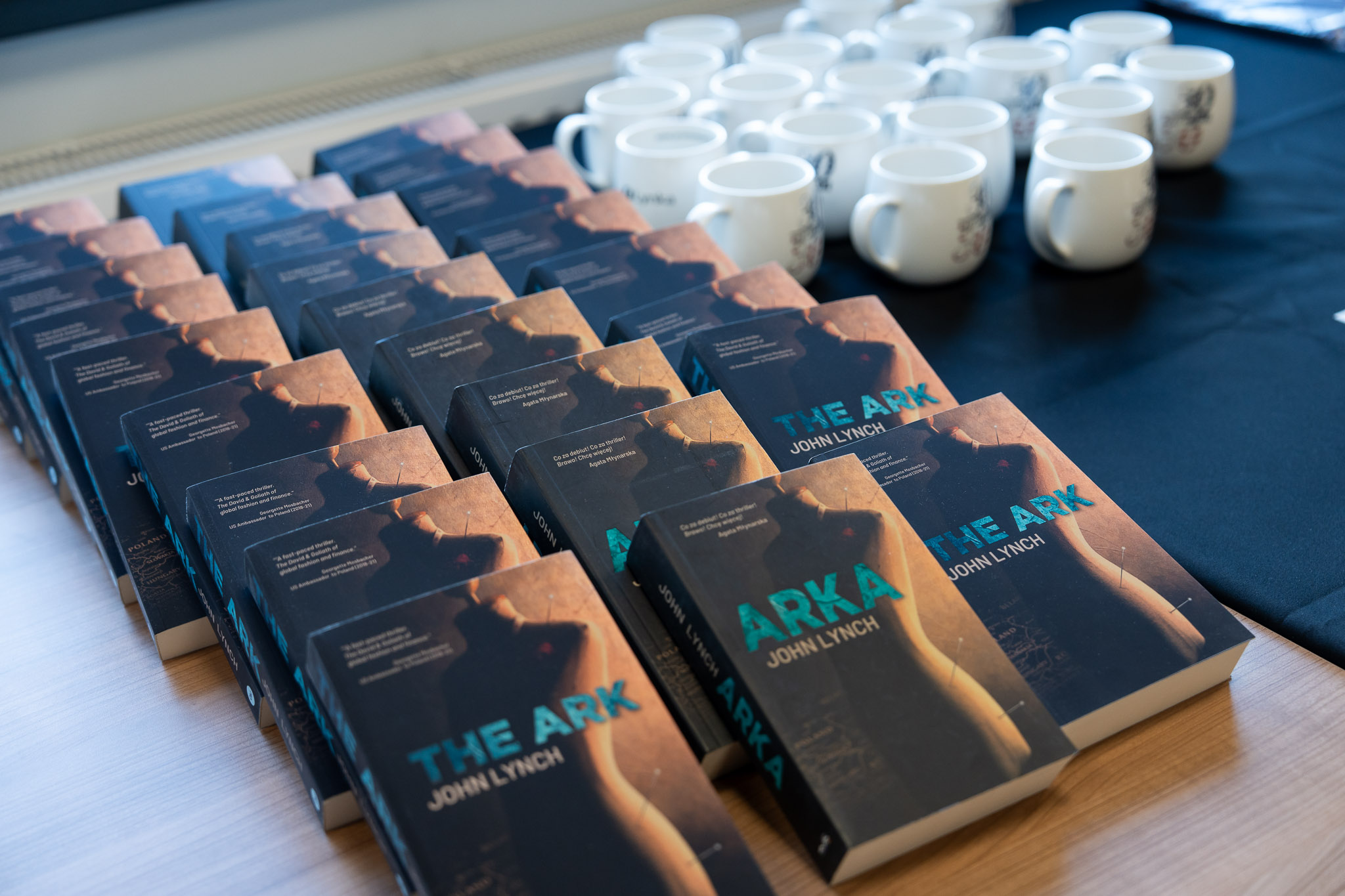 Rzędy książek &bdquo;Arka&rdquo; autorstwa John Lynch ułożone na stole dla uczestnik&oacute;w.