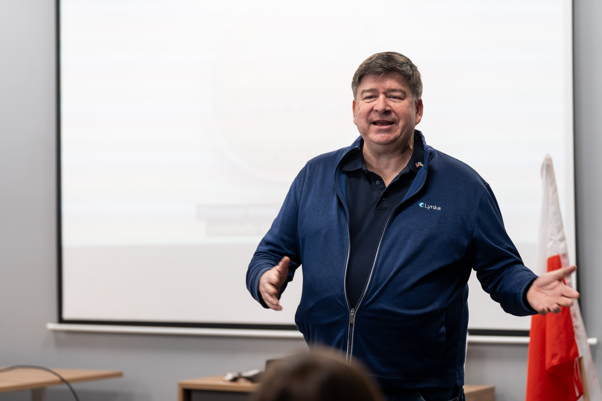 Mężczyzna w granatowej bluzie gestykulujący podczas prowadzenia prelekcji