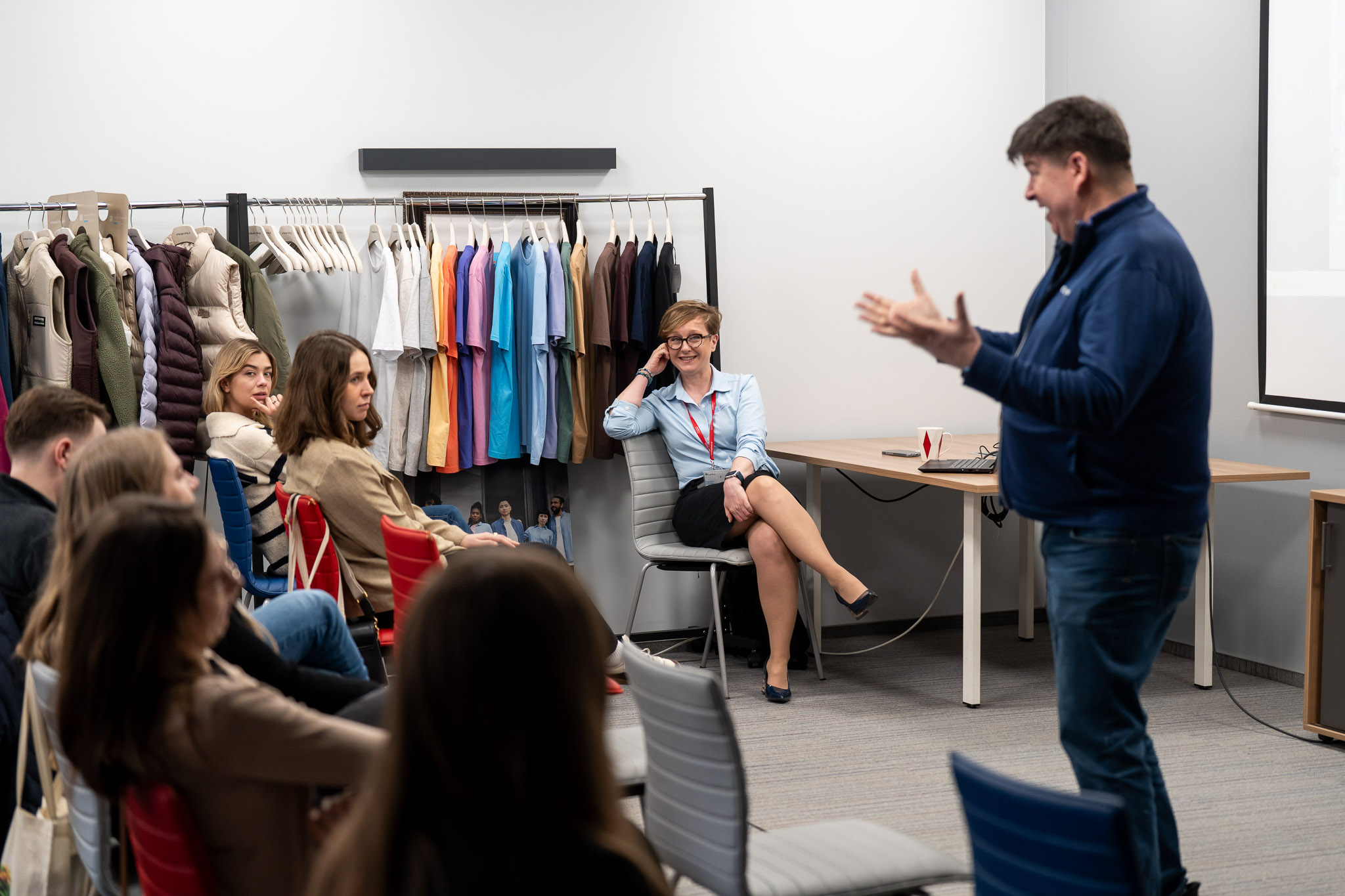 Interakcja prelegenta z grupą w sali wypełnionej materiałami promocyjnymi.