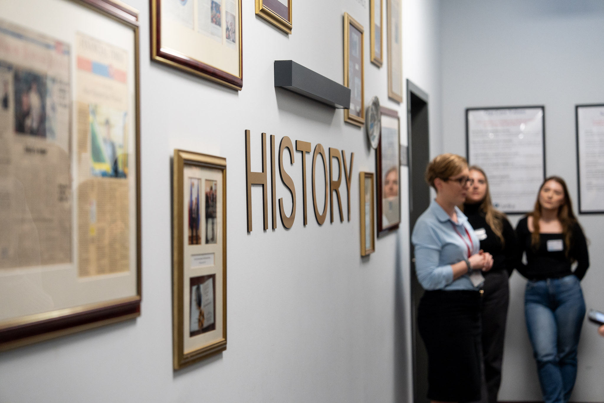 Uczestnicy oglądający galerię zdjęć i napis &bdquo;HISTORY&rdquo; na ścianie biura.