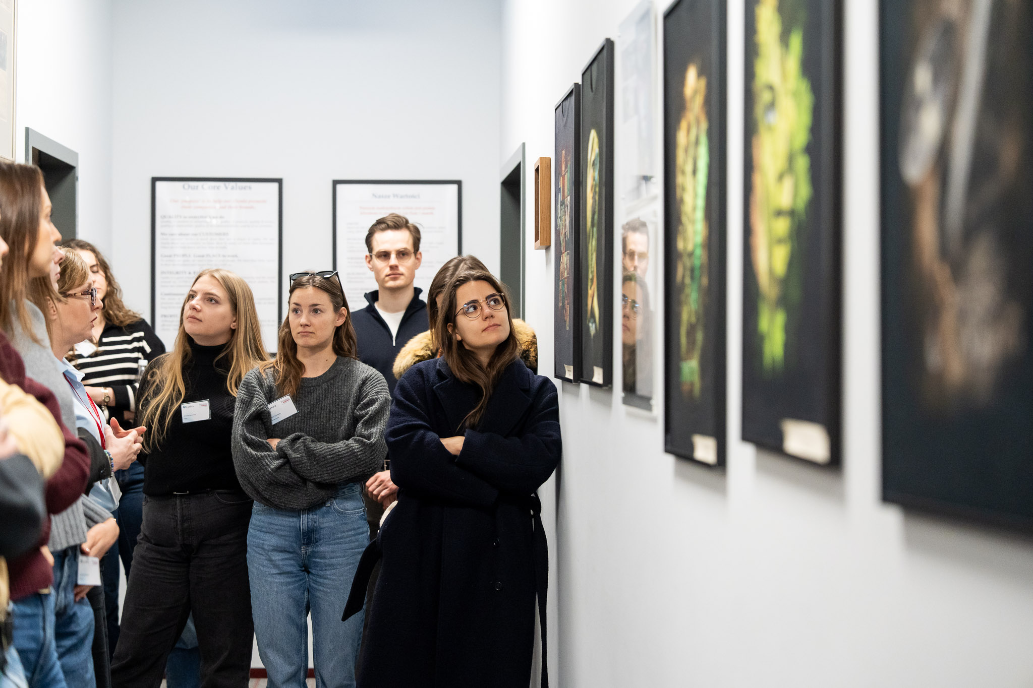 Grupa młodych lider&oacute;w oglądająca obrazy w korytarzu biurowym.
