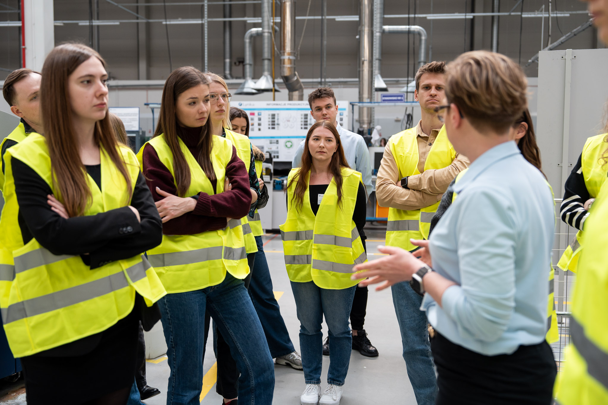 Kobieta w błękitnej koszuli objaśniająca procesy logistyczne grupie w kamizelkach.