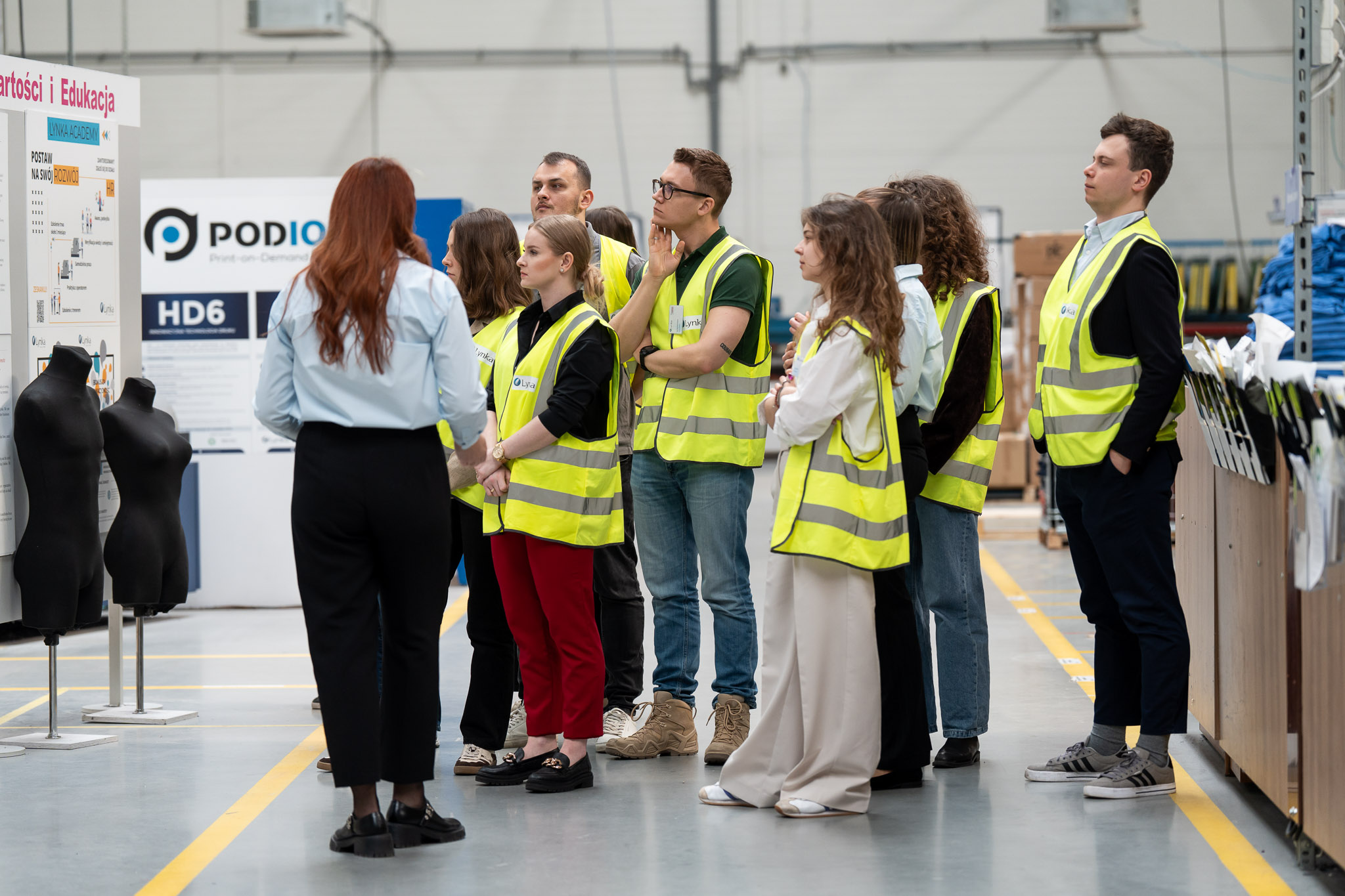 Szerokie ujęcie grupy zwiedzającej nowoczesną halę produkcyjną.