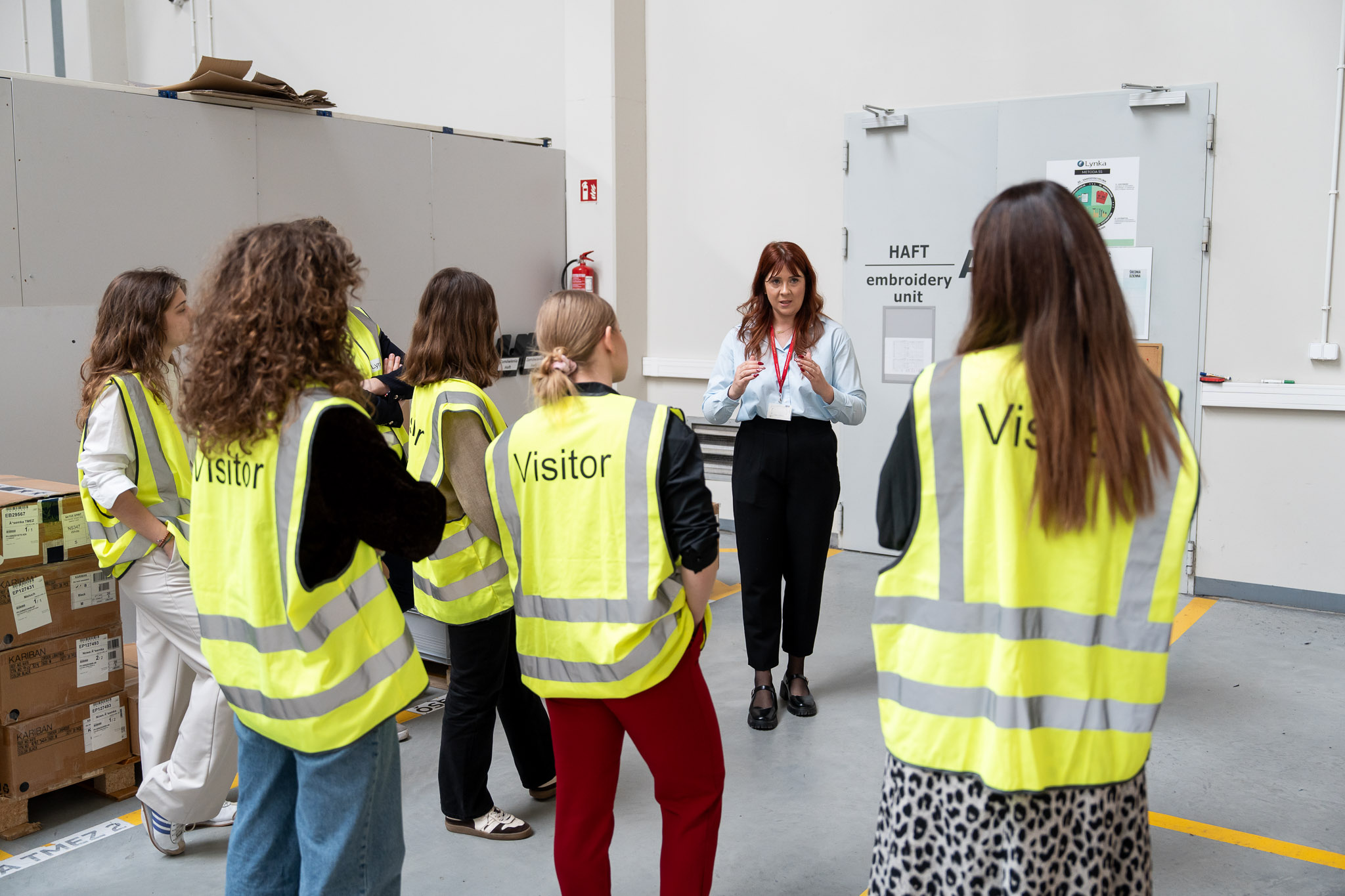 Uczestnicy w kamizelkach odblaskowych dyskutujący wewnątrz zakładu.