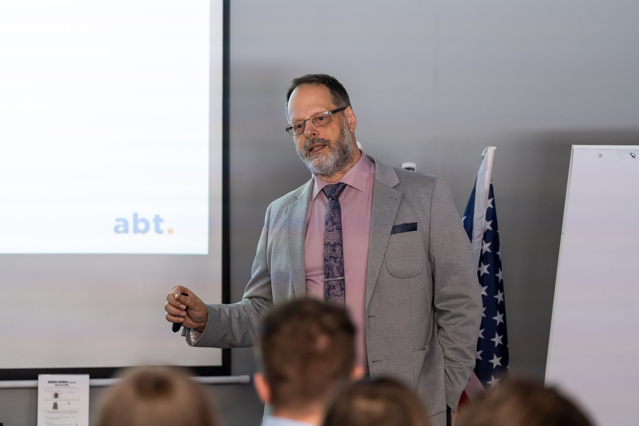 Prelegent w okularach i szarej marynarce przy flipcharcie z logotypem.