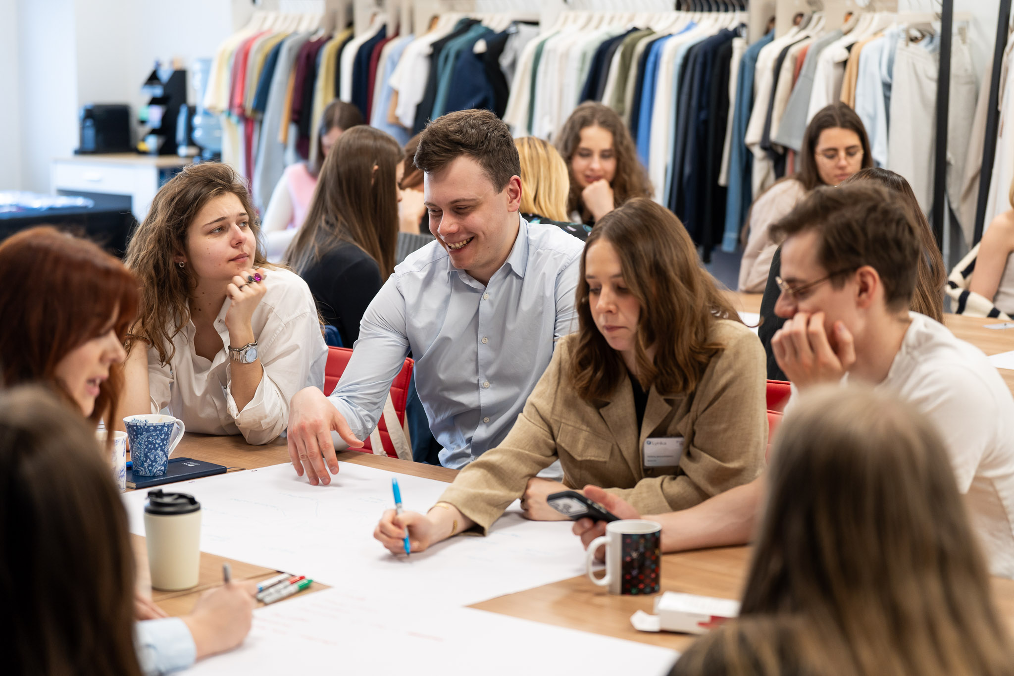 Grupa młodych ludzi wsp&oacute;lnie analizująca projekt przy filiżankach kawy.