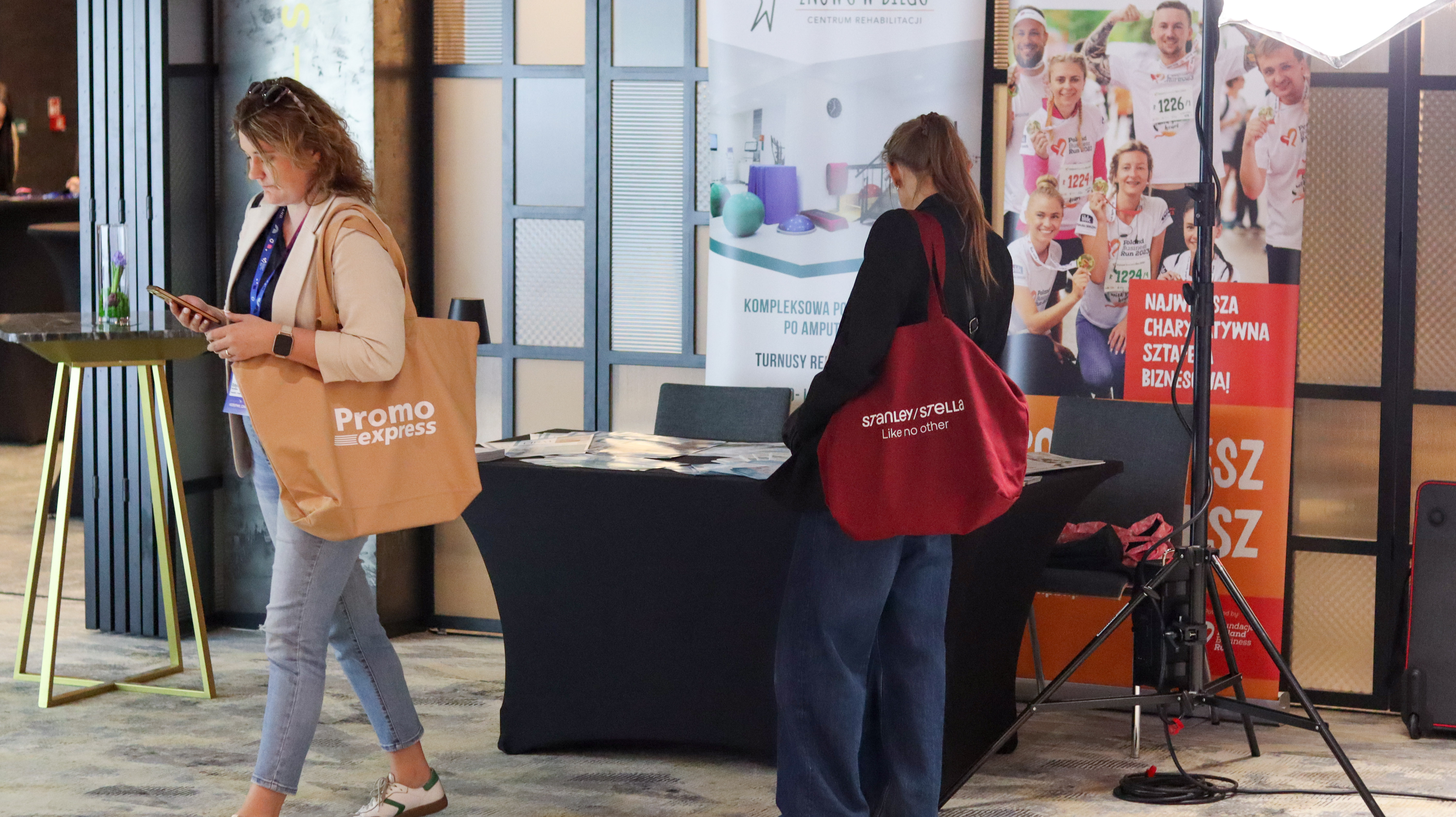 Kobiety przy stoisku. Jedna z beżową torbą promoexpress a druga z bordową torbą Stanley/Stella