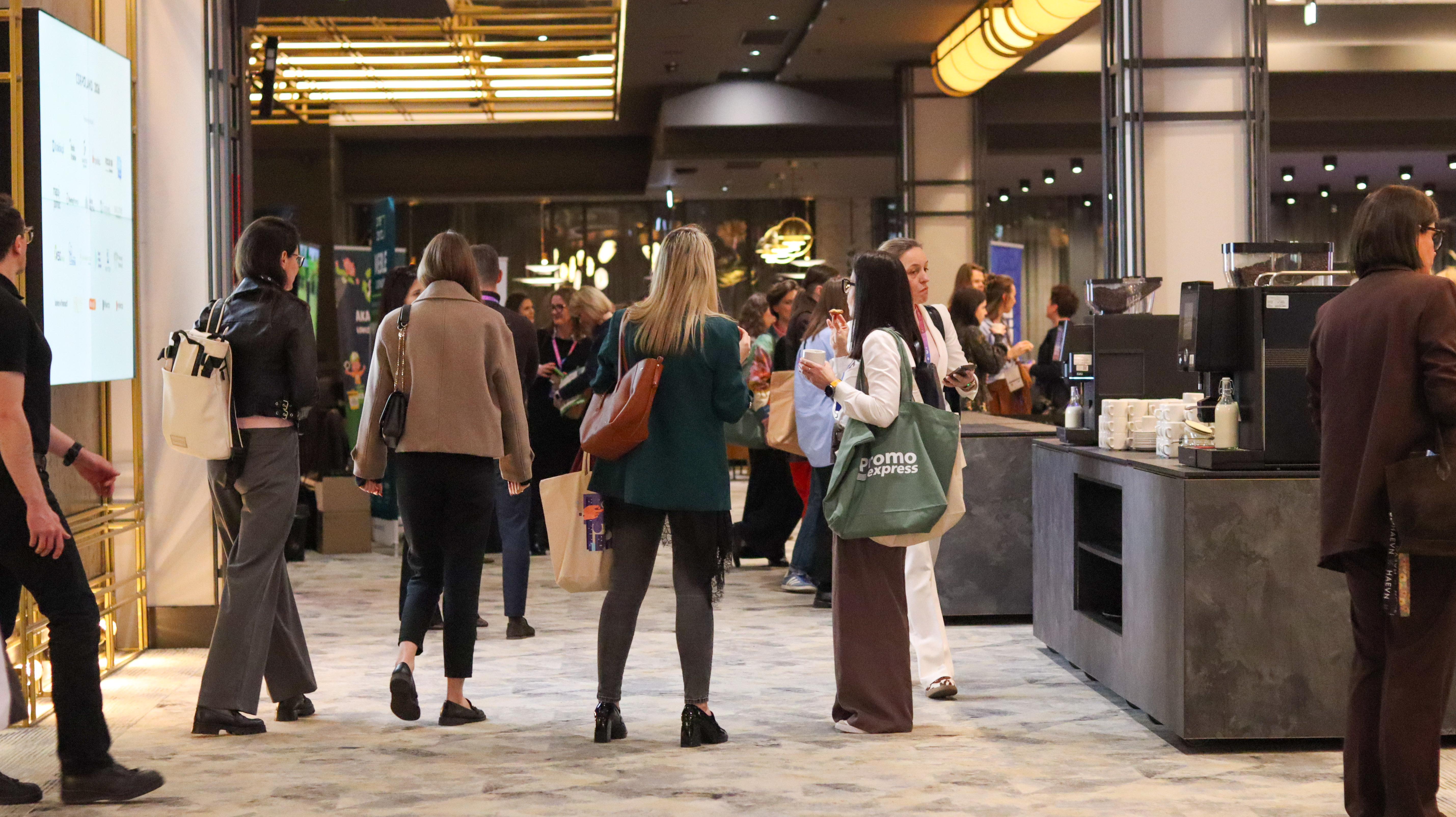 Widok na korytarz konferencyjny. Uczestnicy chodzą lub stoją w grupach.
